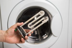 A person holds in his hand a damaged electric heating element from the washing machine. Repair and restoration work
