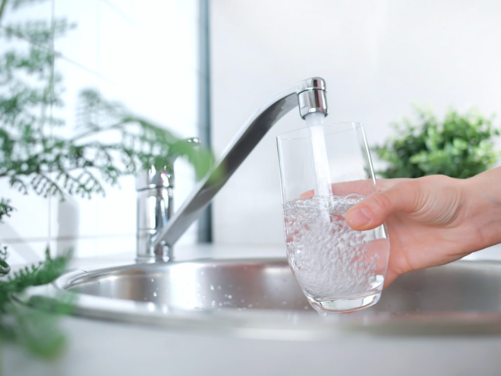 A stream of clean water drink flows into the glass. Woman holding a glass of water under running water from the tap in the kitchen.