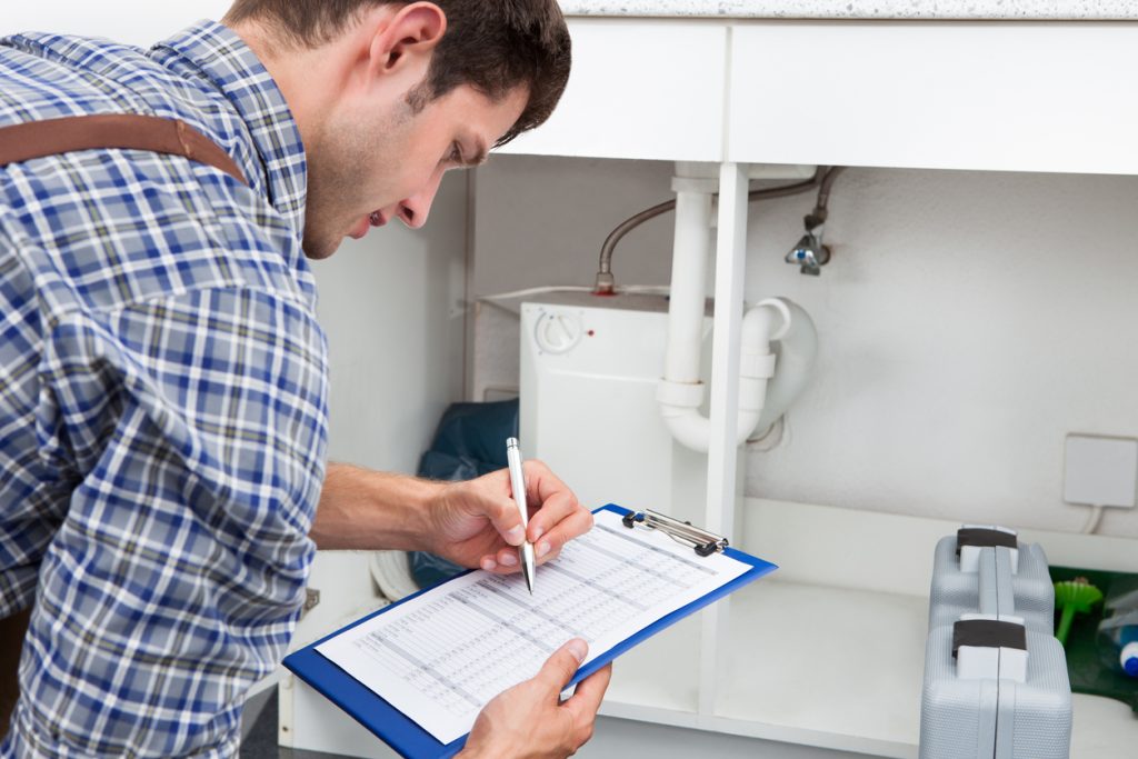 Handsome Young Plumber Writing On Clipboard With Pen In Kitchen Room
